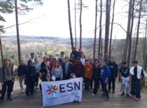 A large group of people standing on the hill in the middle of the forest and holding a white flag with a crest.