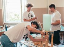 Three students construct an artistic installation from wood and plastic panels.