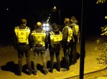 5 students standing the night in front of the oncoming car, students with bright vests and a Tvirtovas written on the back