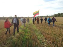 A group of students marching across the field and carrying the Lithuanian flag.