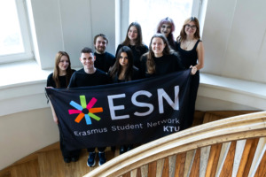 ESN team photo Group of people in the middle of stairs holding a flag and smilling. Behind them two windows.