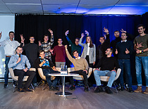 A group photo with enthusiastic participants posing on stage after the event. A relaxed and joyful team atmosphere is visible.