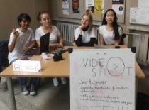 Three girls and one guy are sitting at a table with a poster inviting students to join the VideoShot organization.