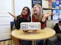 Two girls posing at a table, holding a VideoShot display in their hands.