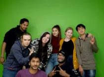 Eight students posing for a photographer at a green wall.