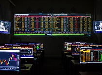 A room with several desks and screens displaying Bloomberg terminal software, financial market charts, and index information. The screen showcases a view of global economic data.