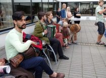 Students with various musical instruments sit in the courtyard of the Faculty of Electrical and Electronics. In the distance, the women listen to the music being performed and the two guys greet.