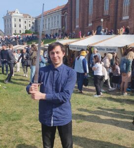 A guy with blue shirt standing with a sword in the n the medieval town in Kaunas days celebration.