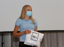 The student holds a white KTU bag in a blue T-shirt with a mask covering her mouth and nose.
