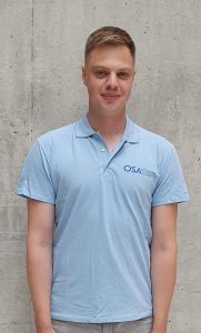 A student with short, blonde hair, in a light blue shirt on a gray background.