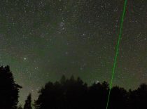 Night, forest and clear, starry sky, and a green laser aimed at the sky.