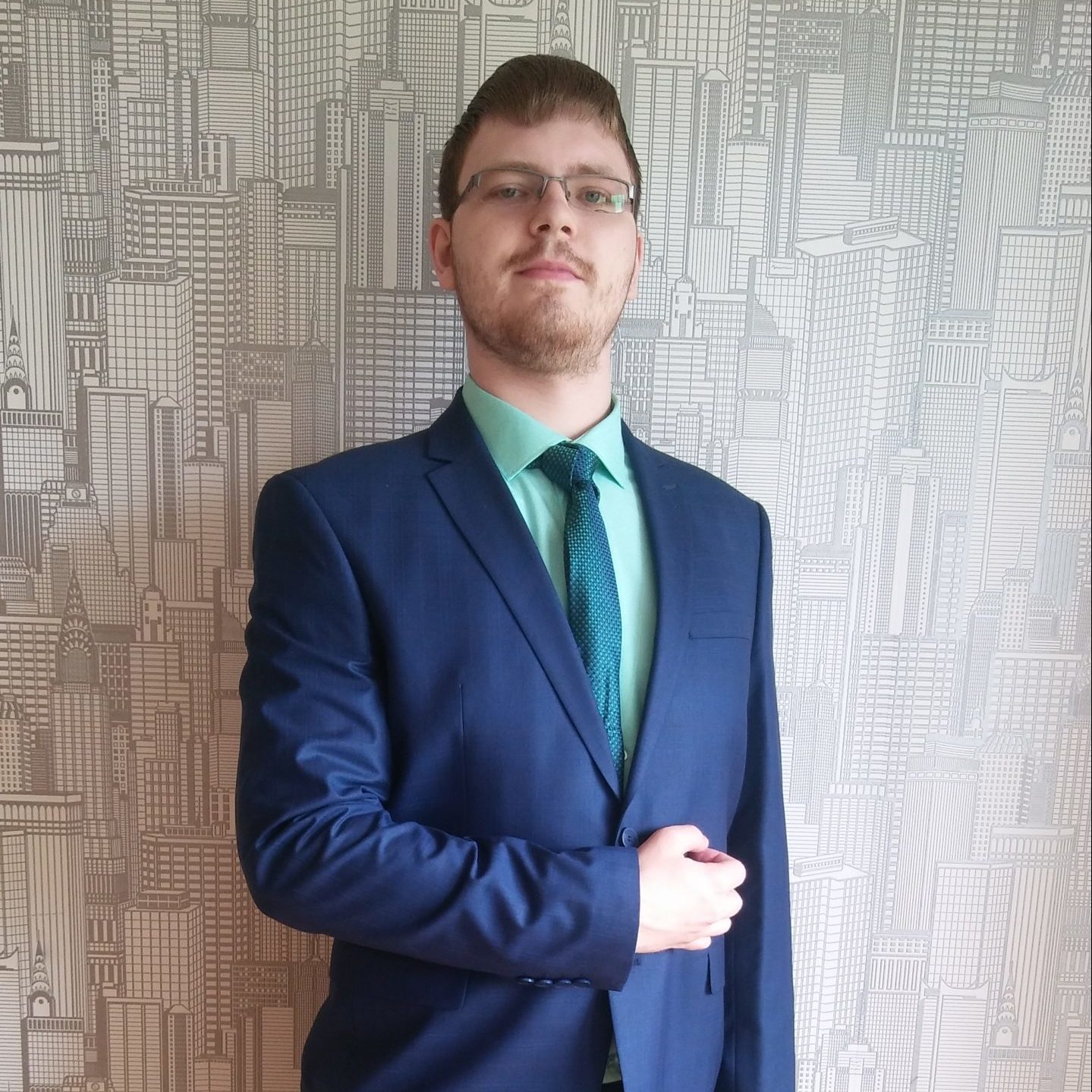 A student with short, dark hair wearing glasses, dressed in a dark blue suit, folded his arm over his elbow.