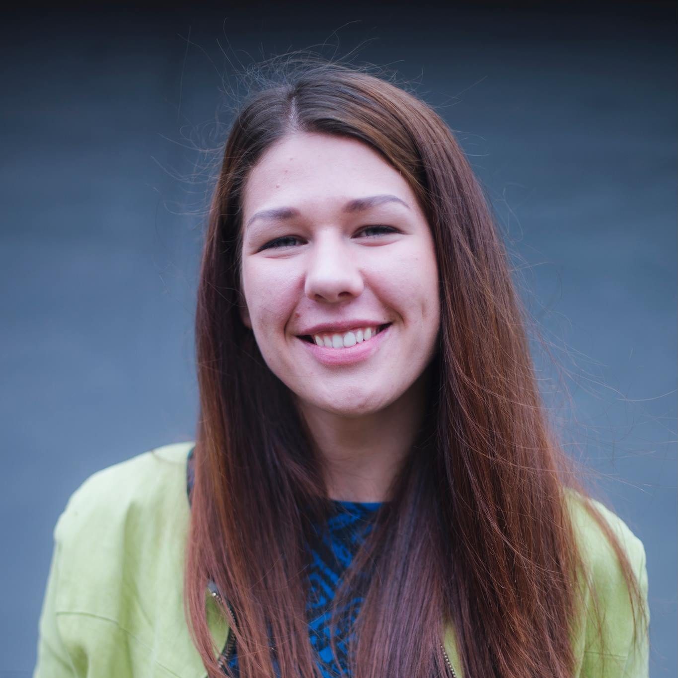 A girl with brown, long hair. He wears a green jacket and a blue shirt