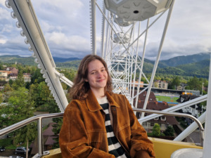 A girl sitting on a carousel, surrounded by a forest and a city.